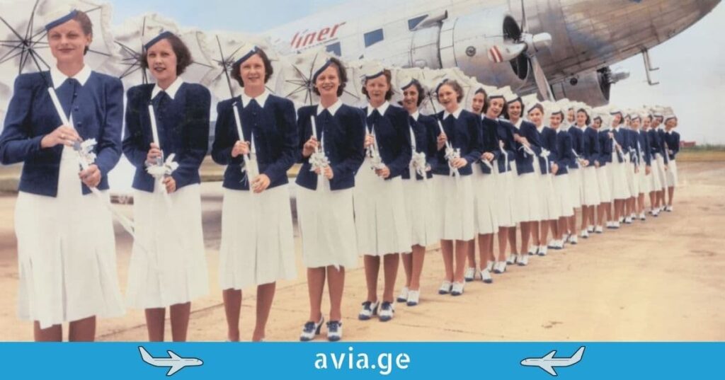 A row of vintage flight attendants in elegant blue and white uniforms holding parasols in front of a classic propeller airplane.