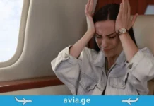 როგორ დავძლიოთ ფრენის შიში – ფსიქოლოგის 5 რჩევა A woman experiencing a panic attack or anxiety due to aerophobia while sitting in an airplane seat next to a window.