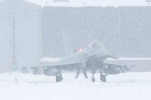 Ground crew working around an Air Baltic plane in heavy snow at the airport.
