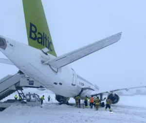 Ground crew clearing snow around an Air Baltic plane at a snowy airport.