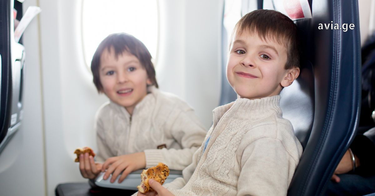 Two young boys sitting in airplane seats and eating snacks during a flight, featuring the Avia.ge logo.