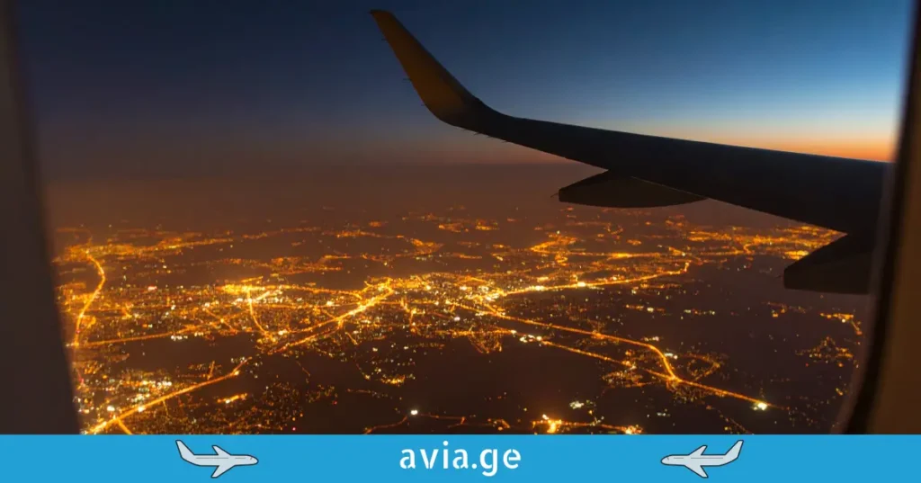 View from airplane window of night city lights with avia.ge branding