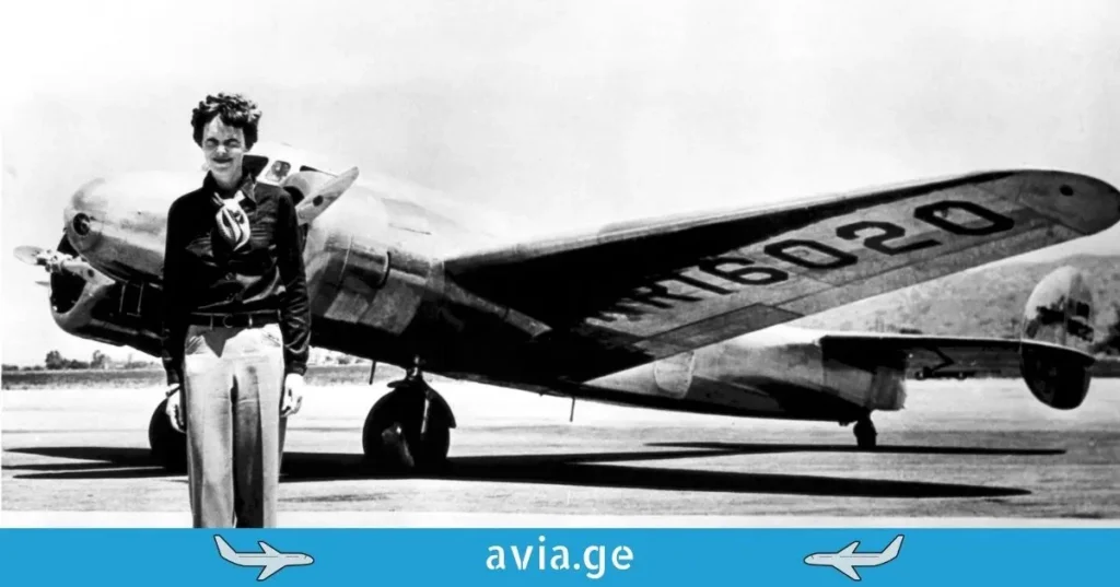 Black and white historical photo of Amelia Earhart posing in front of the wing of her twin-engine Lockheed Electra aircraft, registration NR16020.