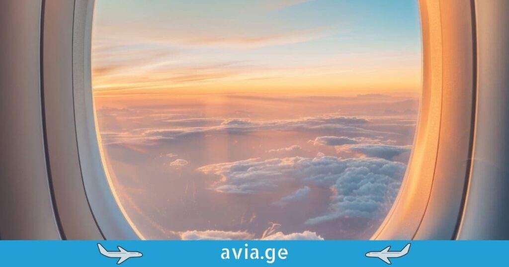 View of a golden sunset over clouds seen through a round airplane window with avia.ge branding at the bottom.