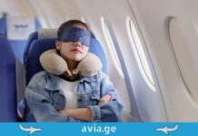 როგორ გავხადოთ ფრენა კომფორტული? აუცილებელი ნივთები მგზავრობისთვის A female passenger sleeping comfortably on a plane using a neck pillow and eye mask.