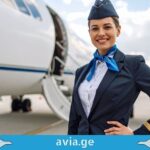 ავიაციის ფარული ენა: რას გვეუბნებიან პილოტები საიდუმლო სიგნალებით? Smiling flight attendant in uniform standing in front of an airplane at the airport with avia.ge logo.