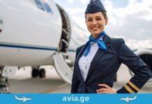 ავიაციის ფარული ენა: რას გვეუბნებიან პილოტები საიდუმლო სიგნალებით? Smiling flight attendant in uniform standing in front of an airplane at the airport with avia.ge logo.