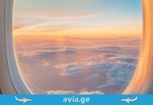 საინჟინრო დეტალები და უსაფრთხოება: რა ვიცით თვითმფრინავის ილუმინატორებსა და მობილურ კავშირზე? View of a golden sunset over clouds seen through a round airplane window with avia.ge branding at the bottom.