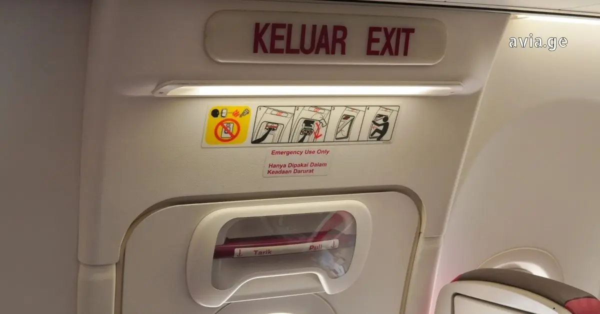 Airplane interior view of an emergency exit door with English and Indonesian text and instructional decals.