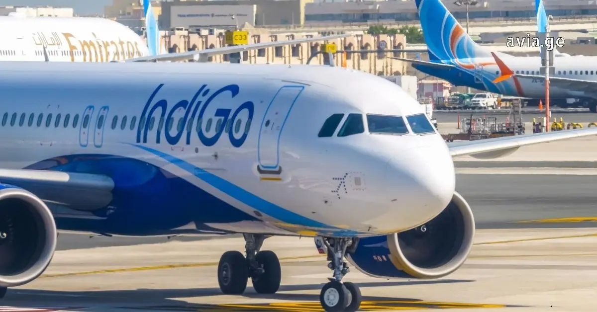 Close-up view of an IndiGo Airlines plane taxiing on the tarmac at an airport, with an Emirates plane tail visible in the background.