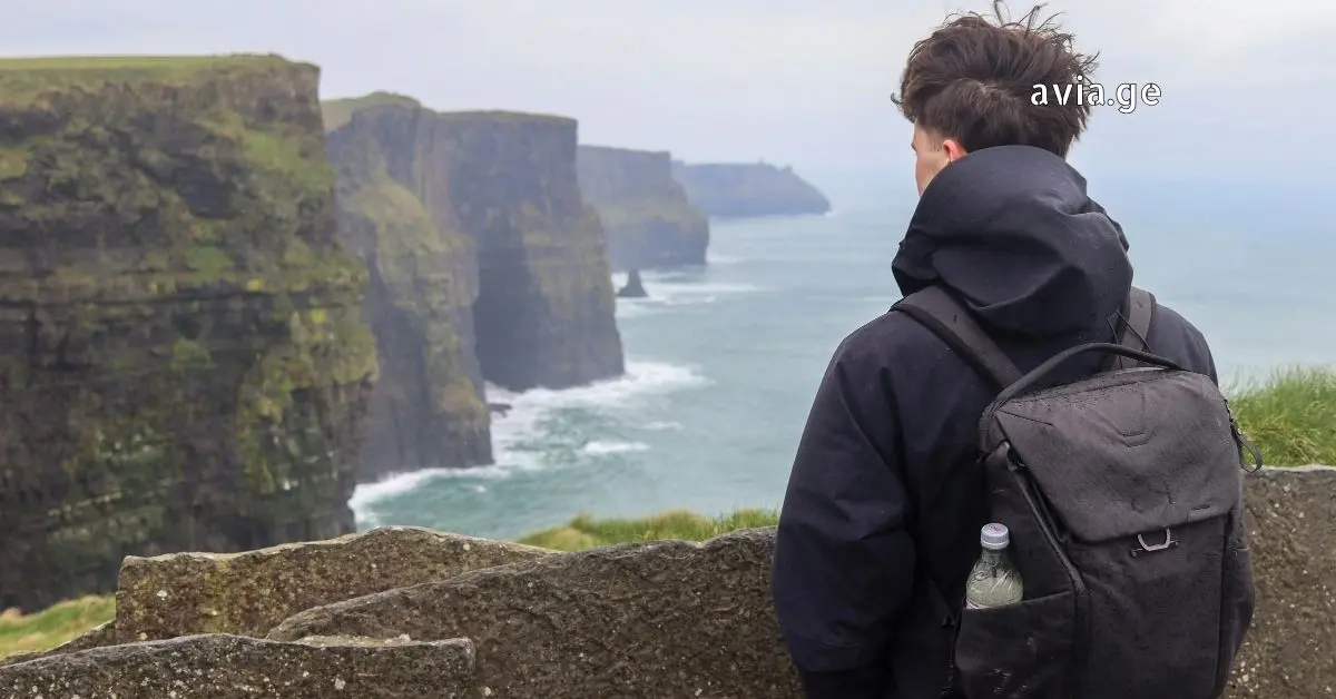A male traveler with a backpack looking out over coastal cliffs.