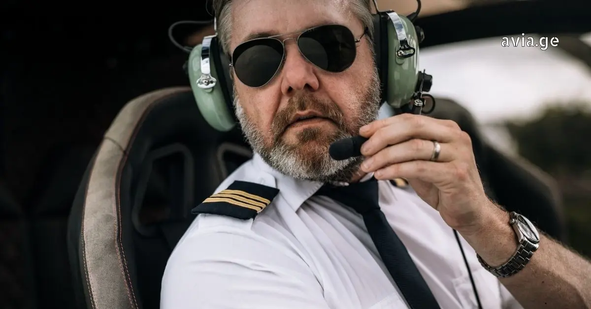 Pilot wearing headset and sunglasses inside helicopter cockpit.