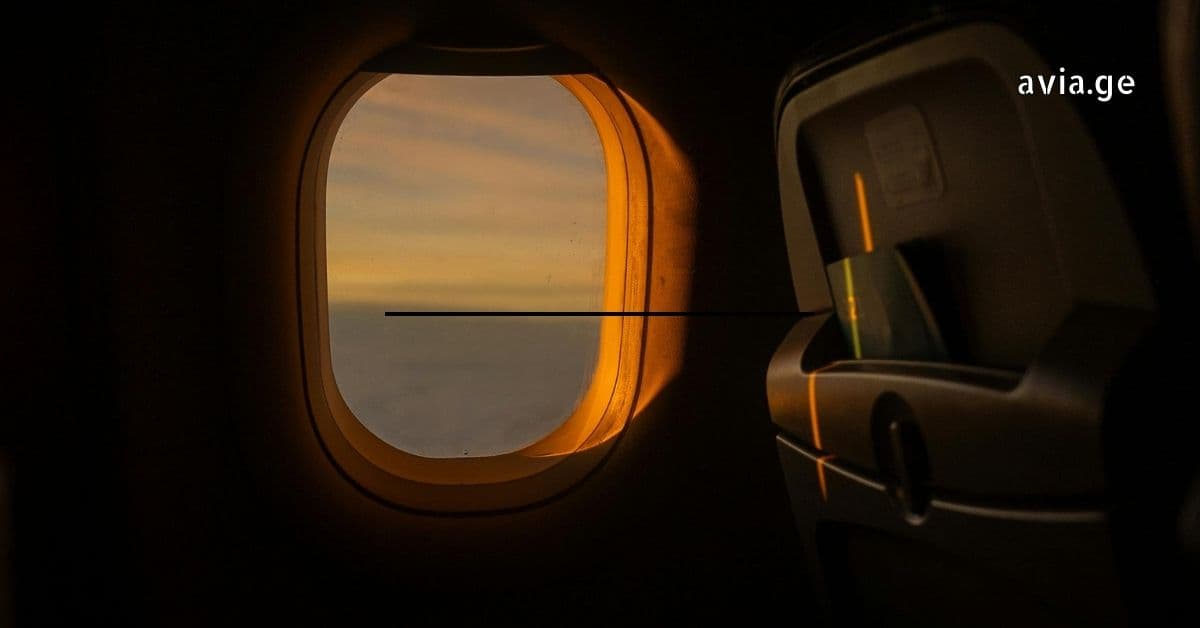 Golden sunset light shining through an airplane window into a dark cabin.