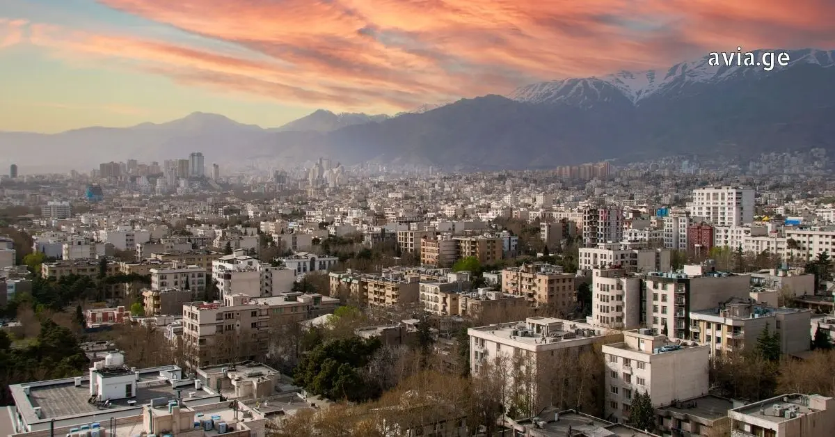 Panoramic aerial view of the Tehran, Iran skyline with snow-capped Alborz Mountains under a sunset sky