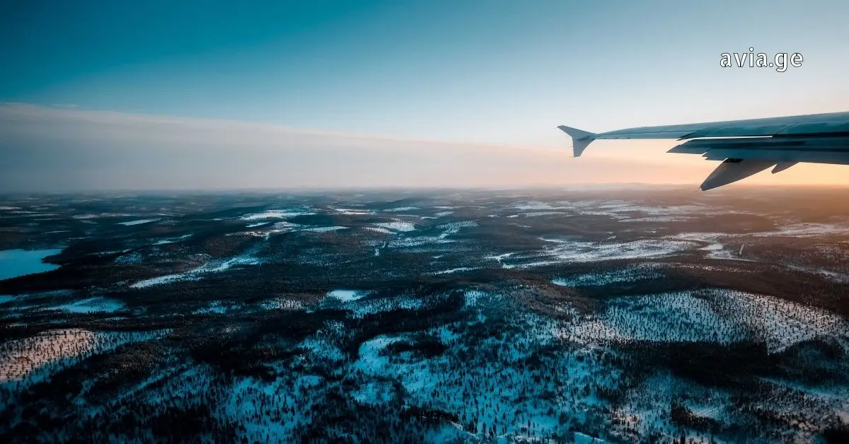 View from an airplane window over a snowy landscape with a wing visible, representing Georgian airspace transit.