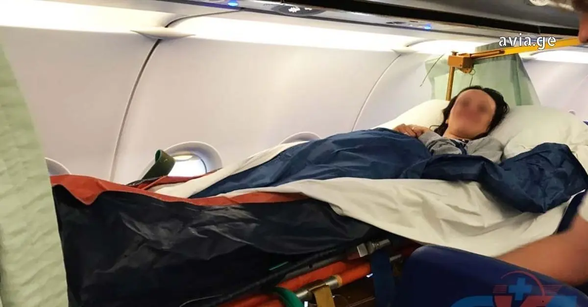 A blurred medical patient lies secured on a specialized stretcher inside a commercial airplane cabin for medical evacuation, attended to by a medical professional.