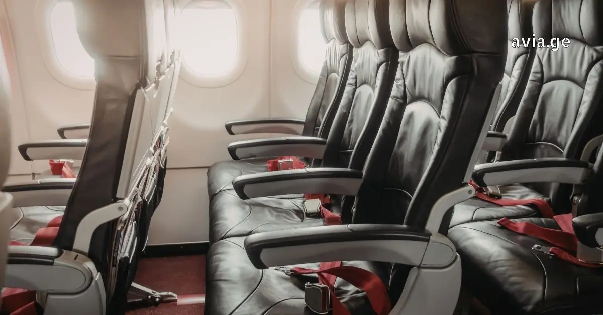 Interior of a commercial airplane cabin showing rows of black leather seats with red seatbelts