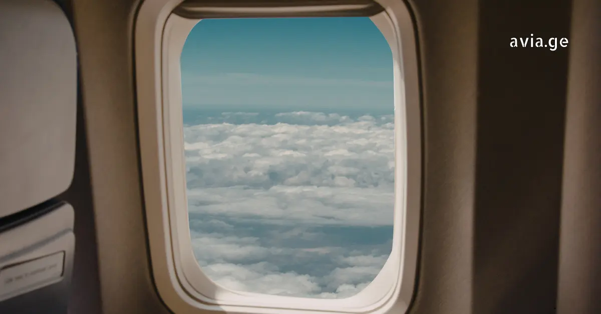 View of white clouds through a round airplane window from the cabin.