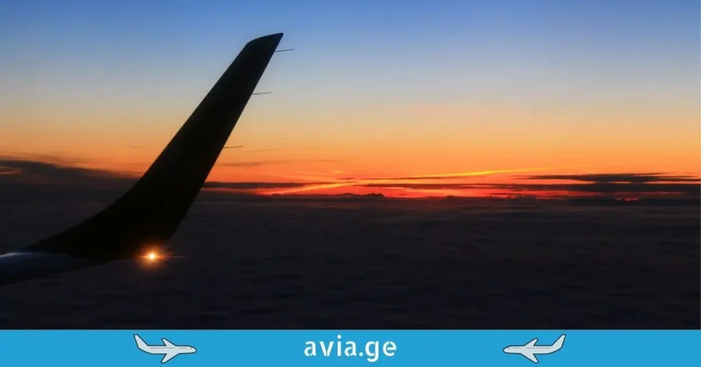 Airplane winglet with lights above clouds at sunset, avia.ge logo.