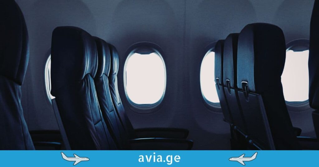 Dark airplane cabin interior with dimmed lights and window views during night flight.