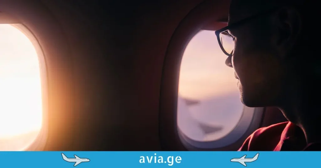 A passenger looking through a round airplane window at sunset.
