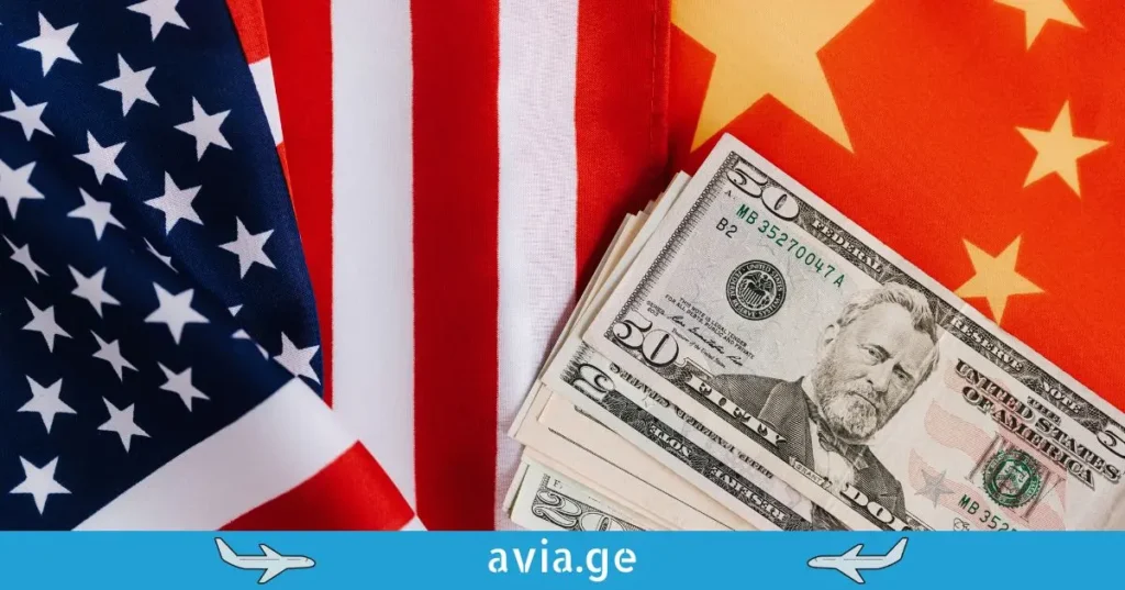 A stack of US dollar bills, with a fifty dollar bill on top, is shown resting on the American and Chinese flags, which are folded next to each other.