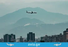 საქართველოს ცა „ოქროს დერეფნად“: რამდენს გამოიმუშავებს ქვეყანა ფრენებიდან A single commercial airplane, labeled with 'aviation', flying at low altitude over a dense urban cityscape with mountains in the background.