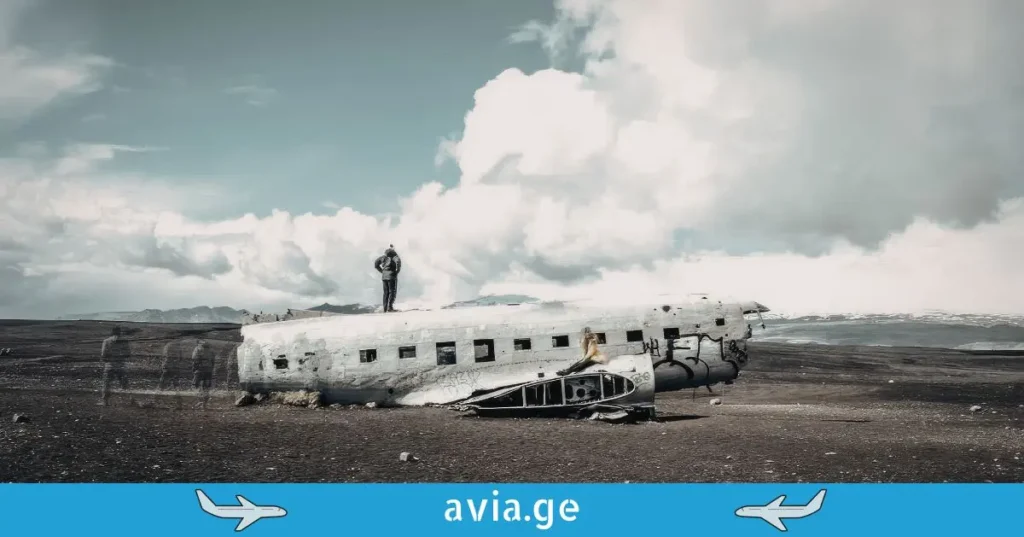 Wreckage of a DC-3 airplane on a volcanic beach in Iceland, with two people posing on it.