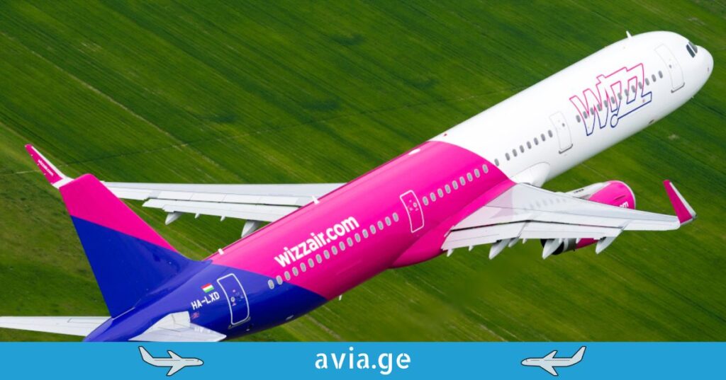 Overhead shot of a Wizz Air Airbus plane flying over a green field