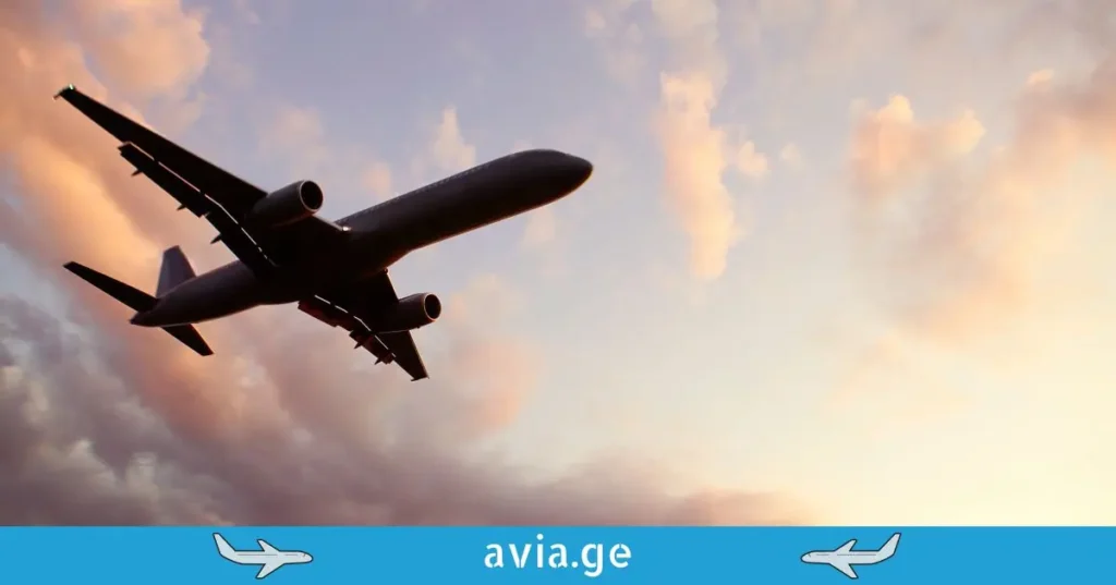 სამგზავრო თვითმფრინავი აფრენისას, ქვედა ხედი, მზის ჩასვლის ღრუბლიანი ცის ფონზე.