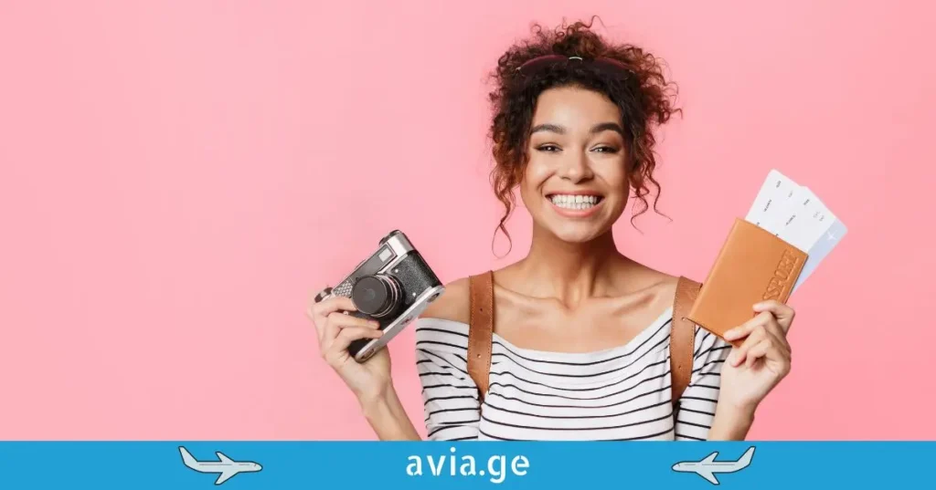 ბედნიერი მოგზაური ქალი კამერით და პასპორტით ვარდისფერ ფონზე -