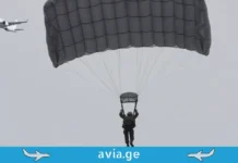 ადამიანი, რომელმაც თვითმფრინავი გაიტაცა და ჰაერში გაქრა პარაშუტისტი ღია ნაცრისფერი პარაშუტით და მფრინავი სამგზავრო თვითმფრინავი ცაში, "avia.ge" ლოგოთი ქვემოთ.