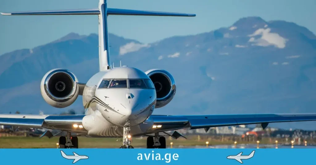 კერძო ბიზნეს ჯეტი ასაფრენ ბილიკზე, მთების ფონზე, avia.ge-ს ლოგოთი.