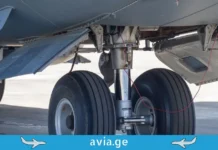 მოზარდი, რომელიც თვითმფრინავის შასის (ბორბლების) განყოფილებაში დაიმალა თვითმფრინავის შასის (ბორბლების) მექანიზმი ახლო ხედით, avia.ge-ს ლოგო